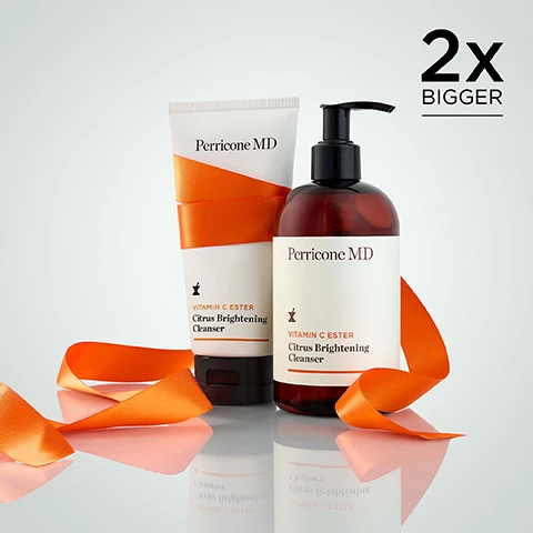 Image 1 - A Perricone MD Vitamin C Ester Citrus Brightening Cleanser tube and a pump bottle are displayed with an orange ribbon on a reflective surface, with the text 2x BIGGER visible in the top right corner. Image 2 - A white product tube with golden liquid product spilling over it, featuring the text Perricone MD, and above it a customer review with five orange stars that reads: After using this product I feel like my skin is clean and refreshed, but it isnt tight or too dry. - LutherChica.